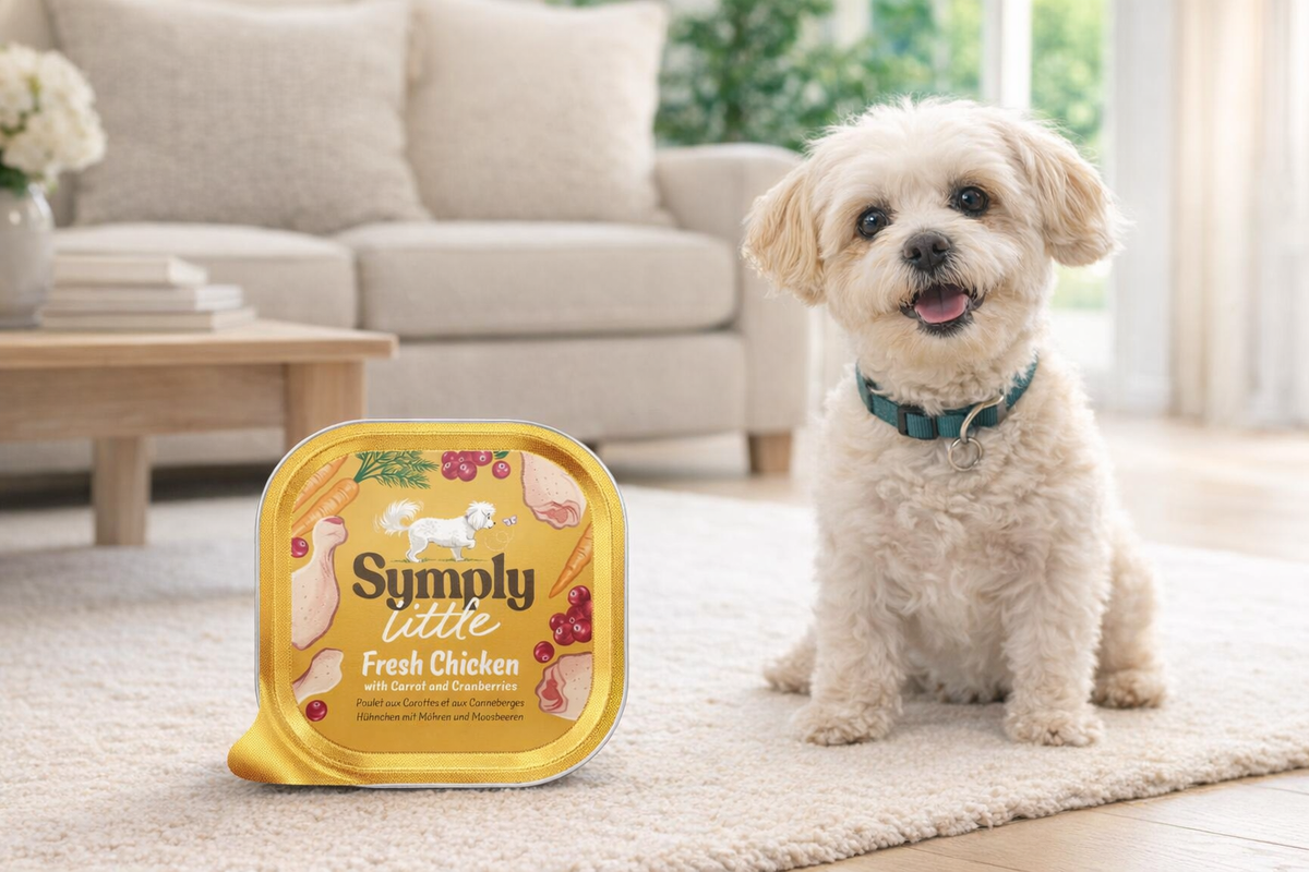 Dog standing next to a 'Simply Tastee' pet food container in a living room setting.
