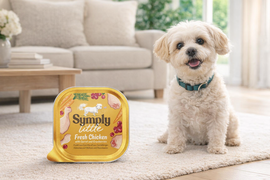 Dog standing next to a 'Simply Tastee' pet food container in a living room setting.