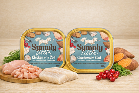 Two tins of 'Simply Little' pet food with ingredients on a wooden surface