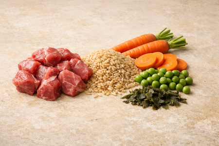Raw meat, rice, carrots, peas, and seaweed on a textured surface