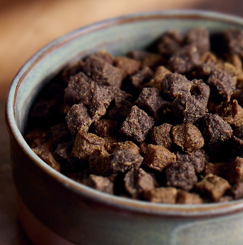 Close-up of a bowl filled with McAdams Air Dried dog food on a wooden surface.