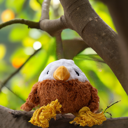 Great & Small Stay Wild Golden Eagle Dog Toy perched in a tree, featuring soft plush fabric and rope legs for outdoor-inspired dog fun.